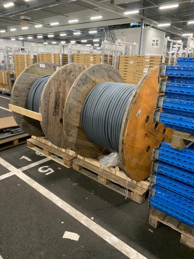 Grote houten spoelen met kabels, geplaatst op een pallet in een magazijn.